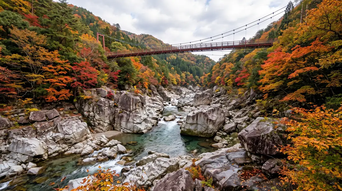 La garganta de Oni-no-Shitaburui en Okuizumo, un cañón de rocas de granito con un río cristalino y un puente colgante cruzando en lo alto, entre laderas teñidas de rojo y naranja en otoño