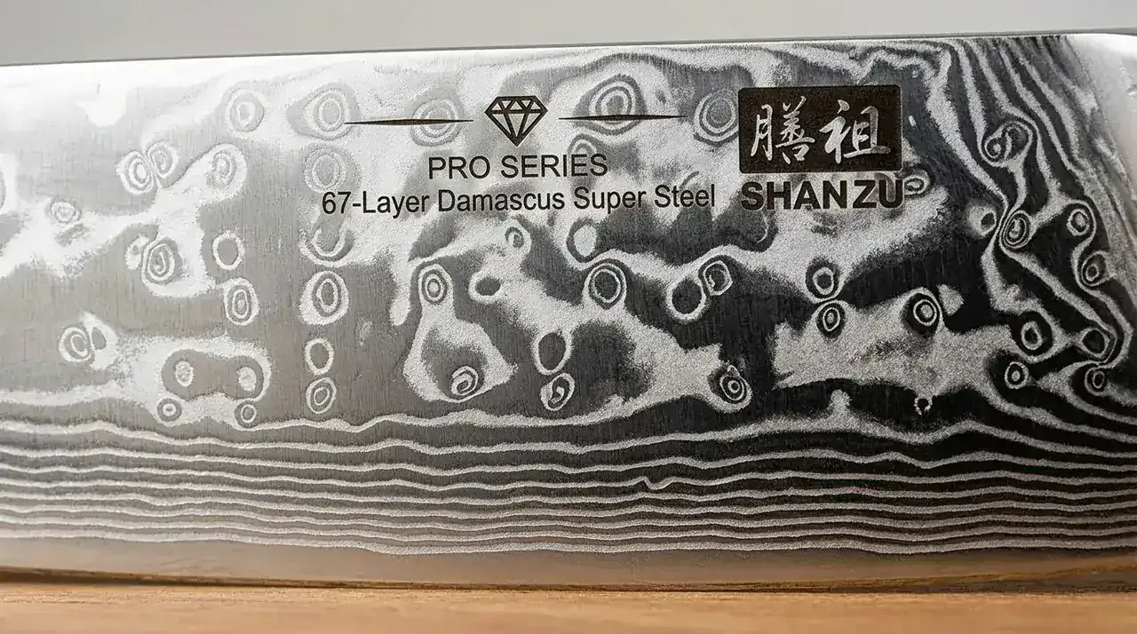 Detalle macro del filo de damasco de 67 capas del SHAN ZU Chef Pro, con el patrón laminado sobre el núcleo