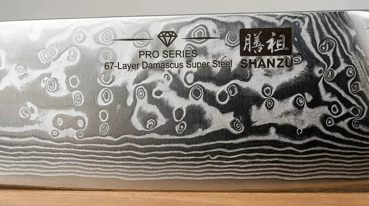 Detalle macro del filo de damasco de 67 capas del SHAN ZU Chef Pro, con el patrón laminado sobre el núcleo